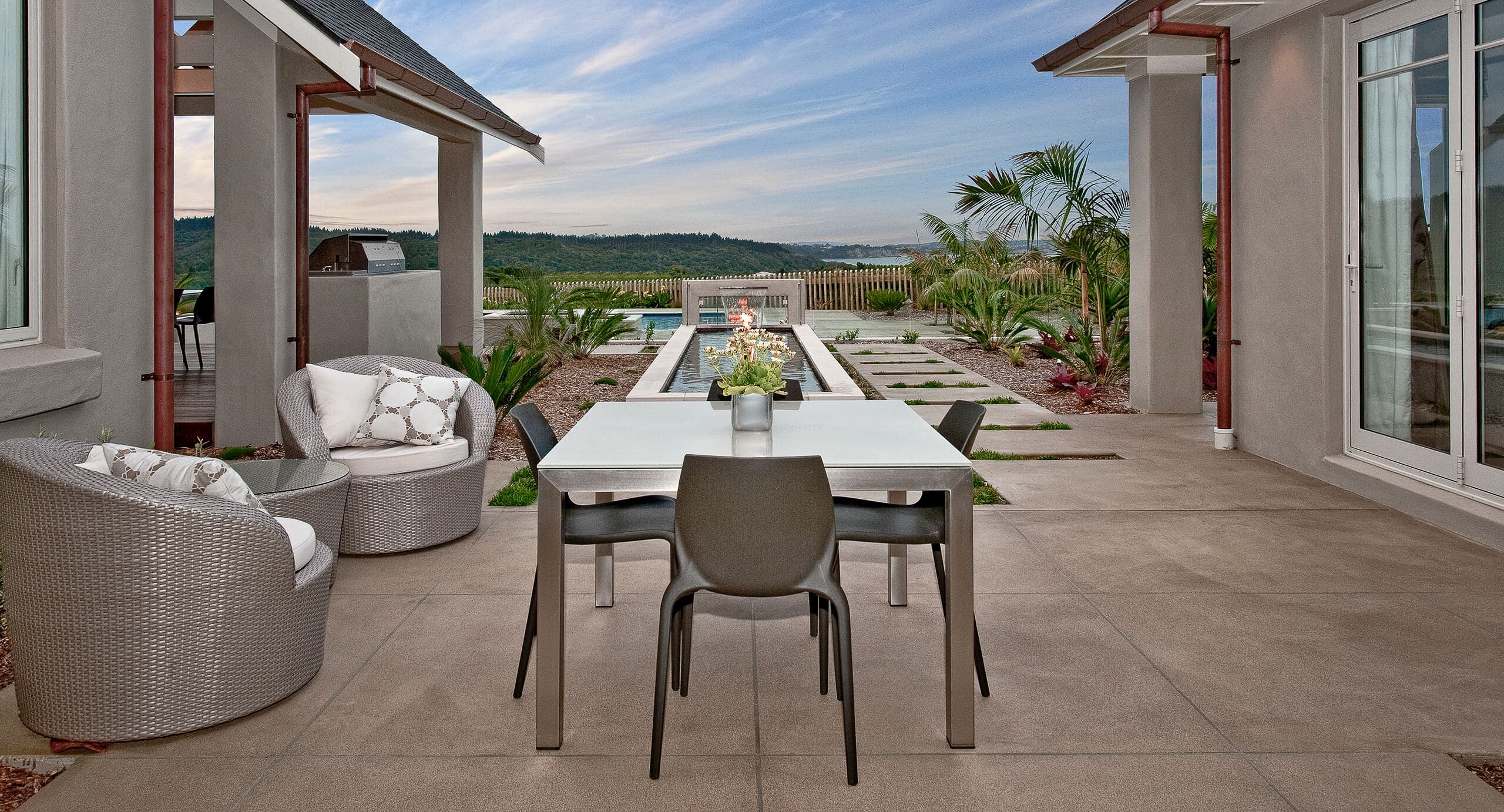 coloured concrete patio with dining table overlooking pool.