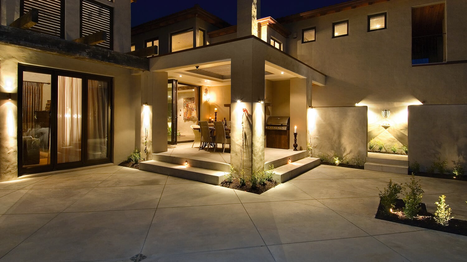 Coloured concrete patio and outdoor dining area under lights at night time.